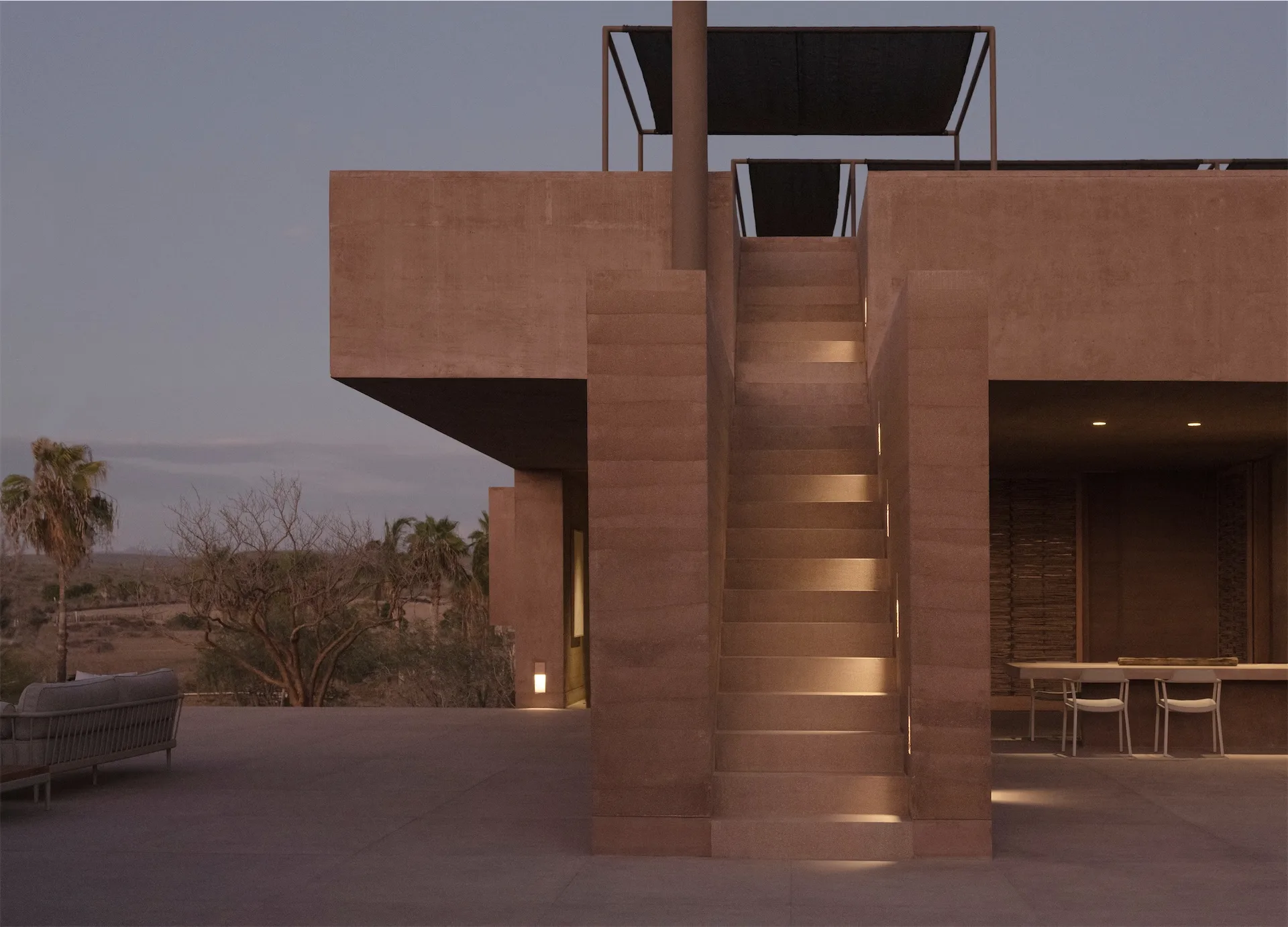 A modern rammed-earth hotel at dusk, stairs lit from below