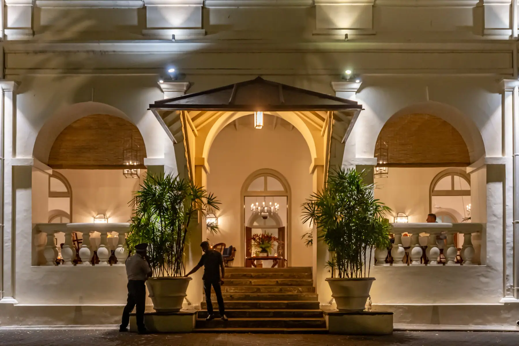 A hotel entrance lit at night, two staff at the steps under the porte-cochere