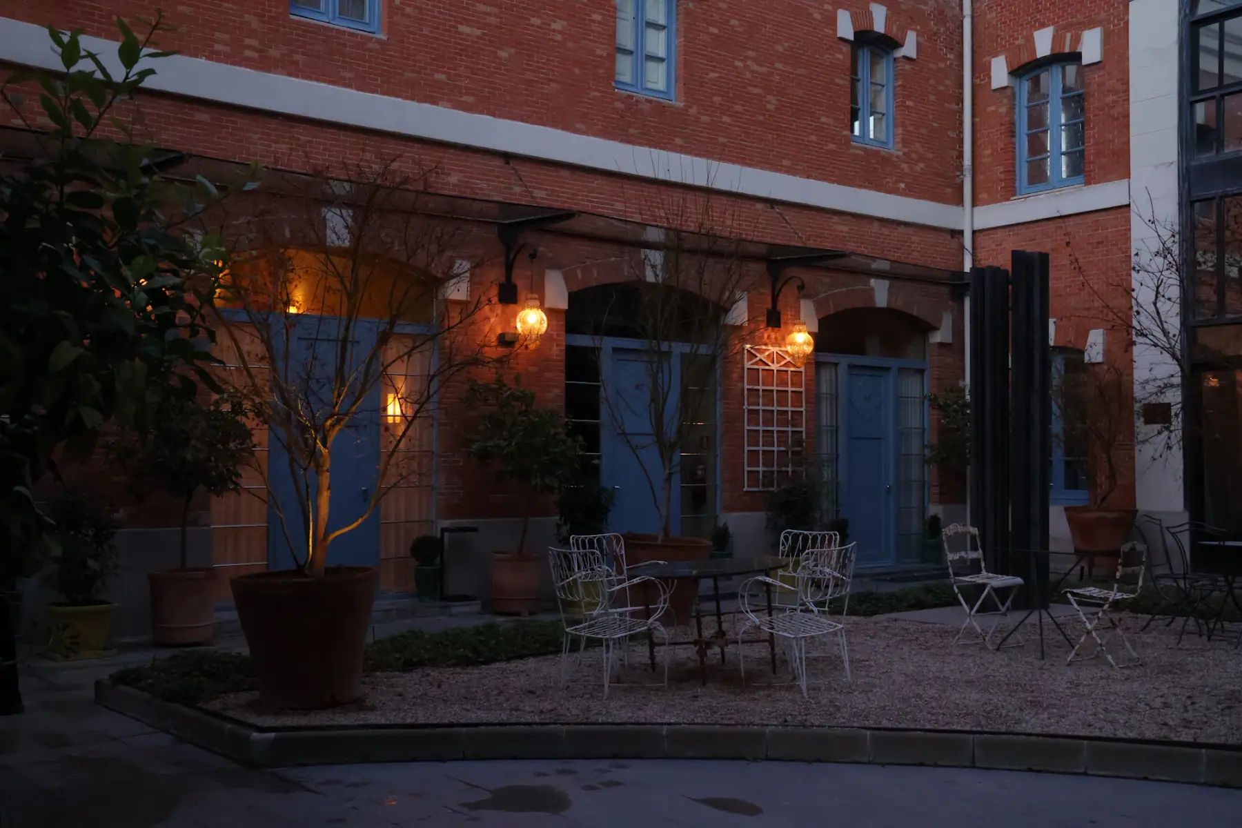 A brick boutique hotel at dusk, its lamps lit above the cafe tables